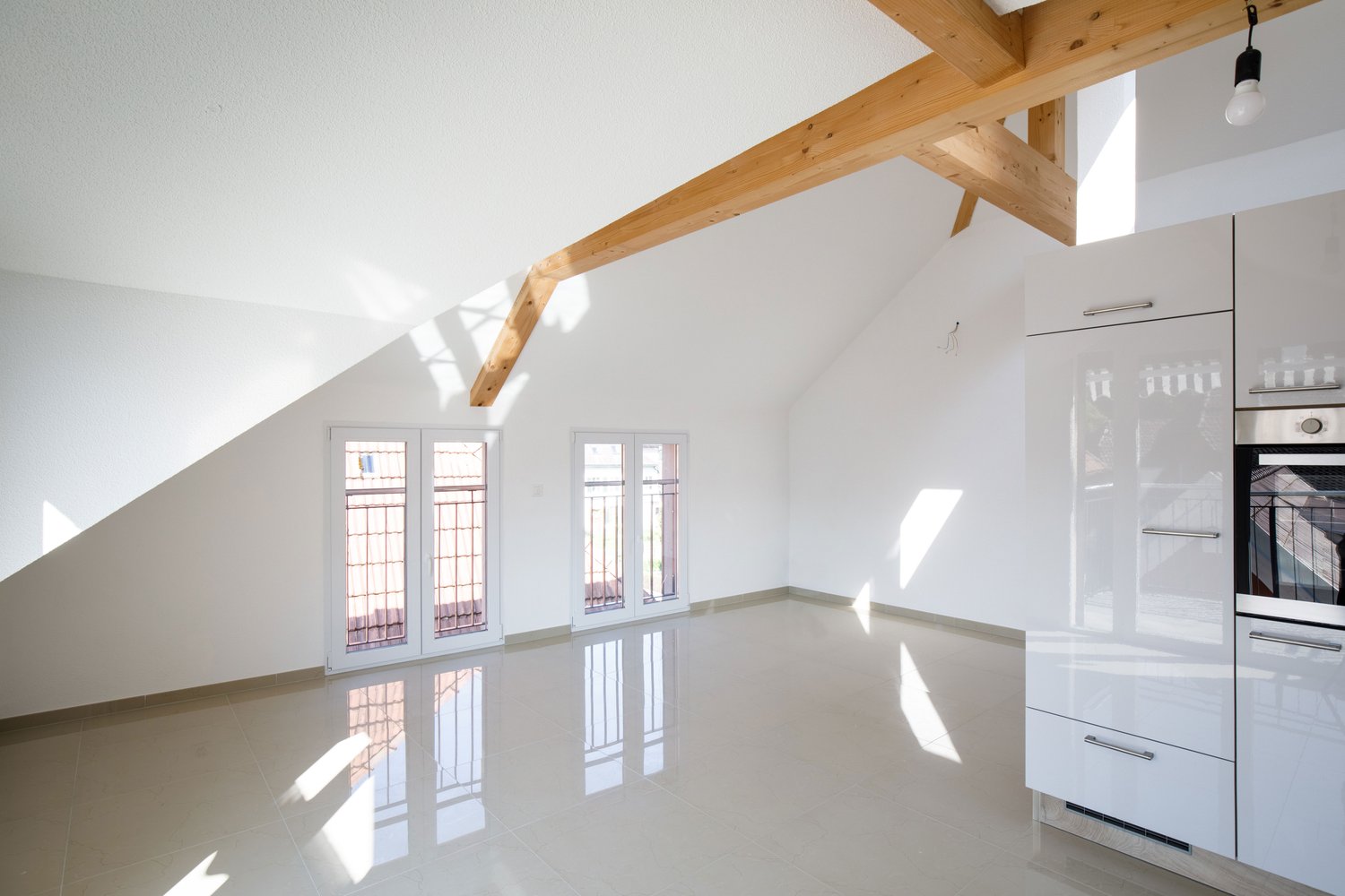 An empty room with wooden beams on the ceiling, white tiles on the floor, and two sets of doors opening to the outside
