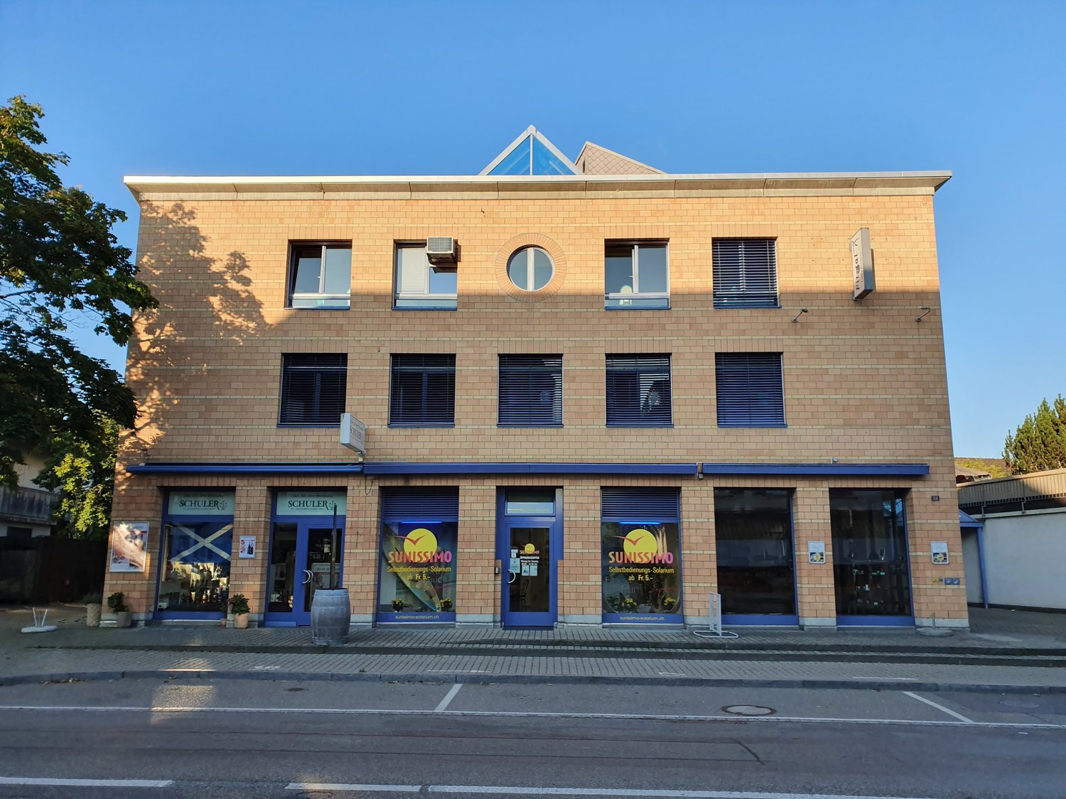 Two story commercial building, brick facade, glass windows, three entrances, sign reading 'Sunissimo'