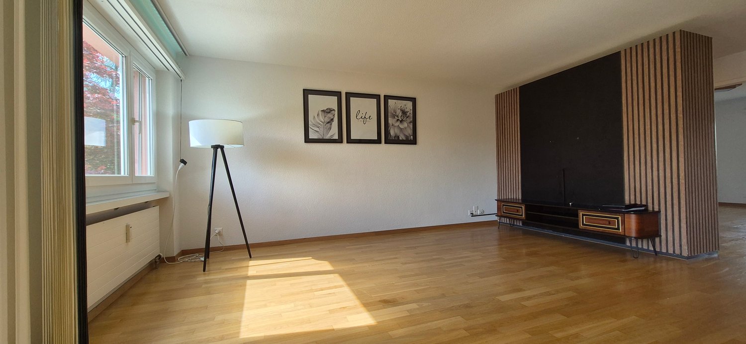 Spacious living room with hardwood floors, large windows, wall decor, and a wooden entertainment unit