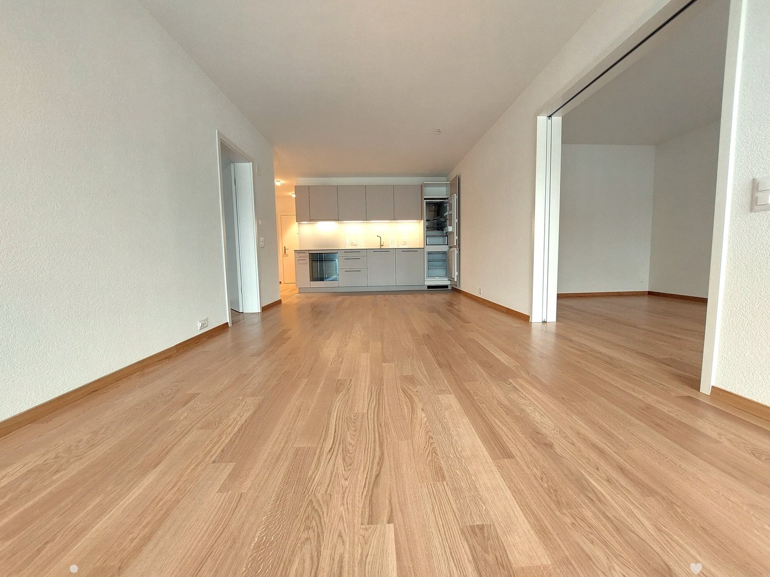 large empty room with kitchen, wooden floor, white walls, cabinet