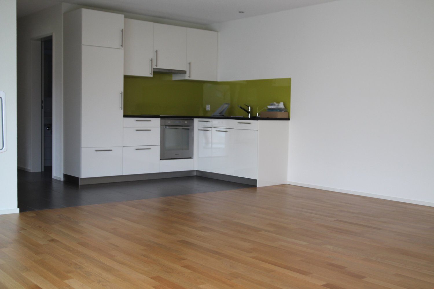 empty kitchen, wooden floor, white walls, green backsplash, stainless steel appliances
