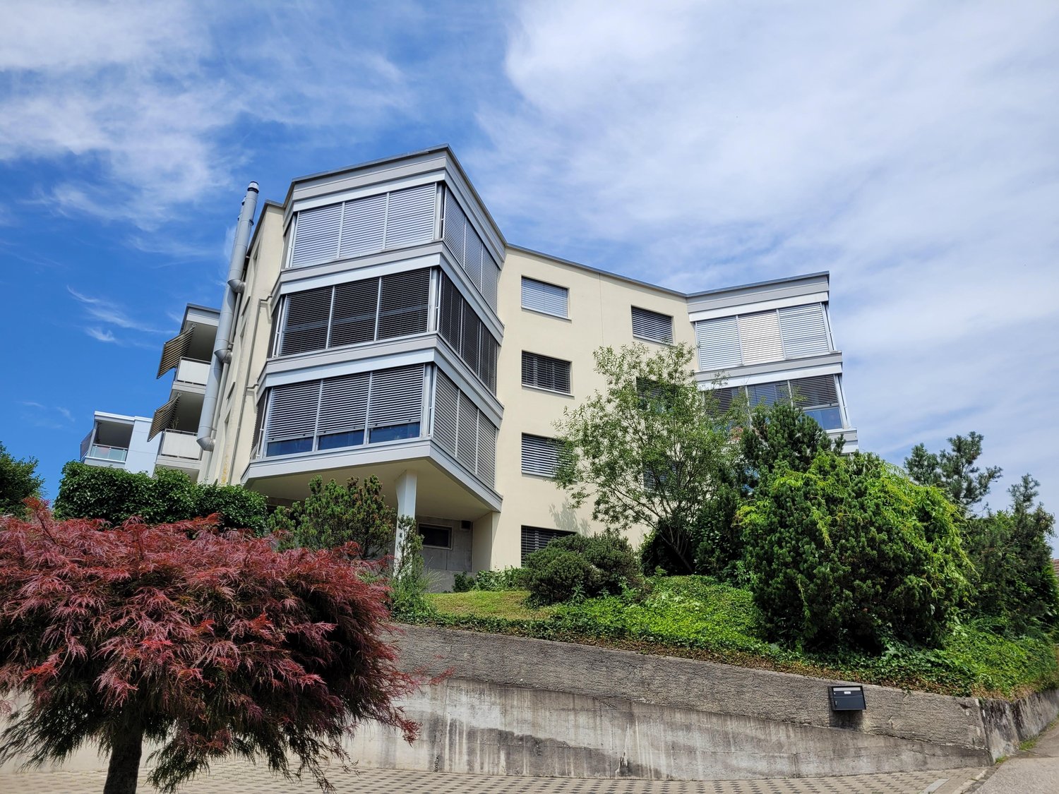 4 story building, balconies, multiple windows, modern design, trees, bushes