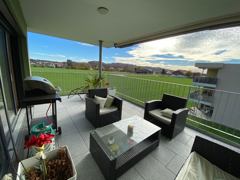 Terrace with outdoor furniture and grill, overlooking a large green field and hills