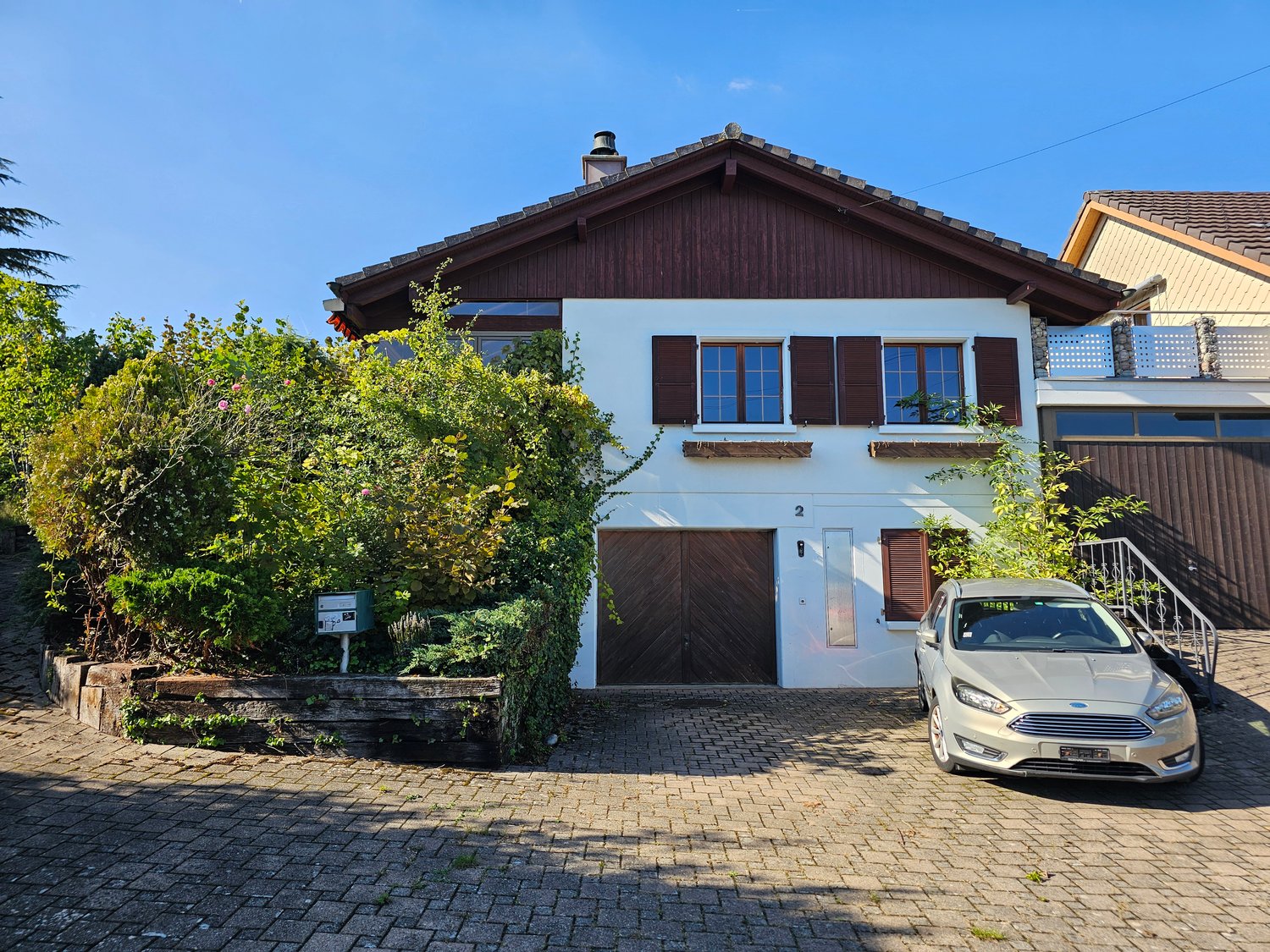 two-story house with a chimney, brown wooden exterior, wooden garage, white base