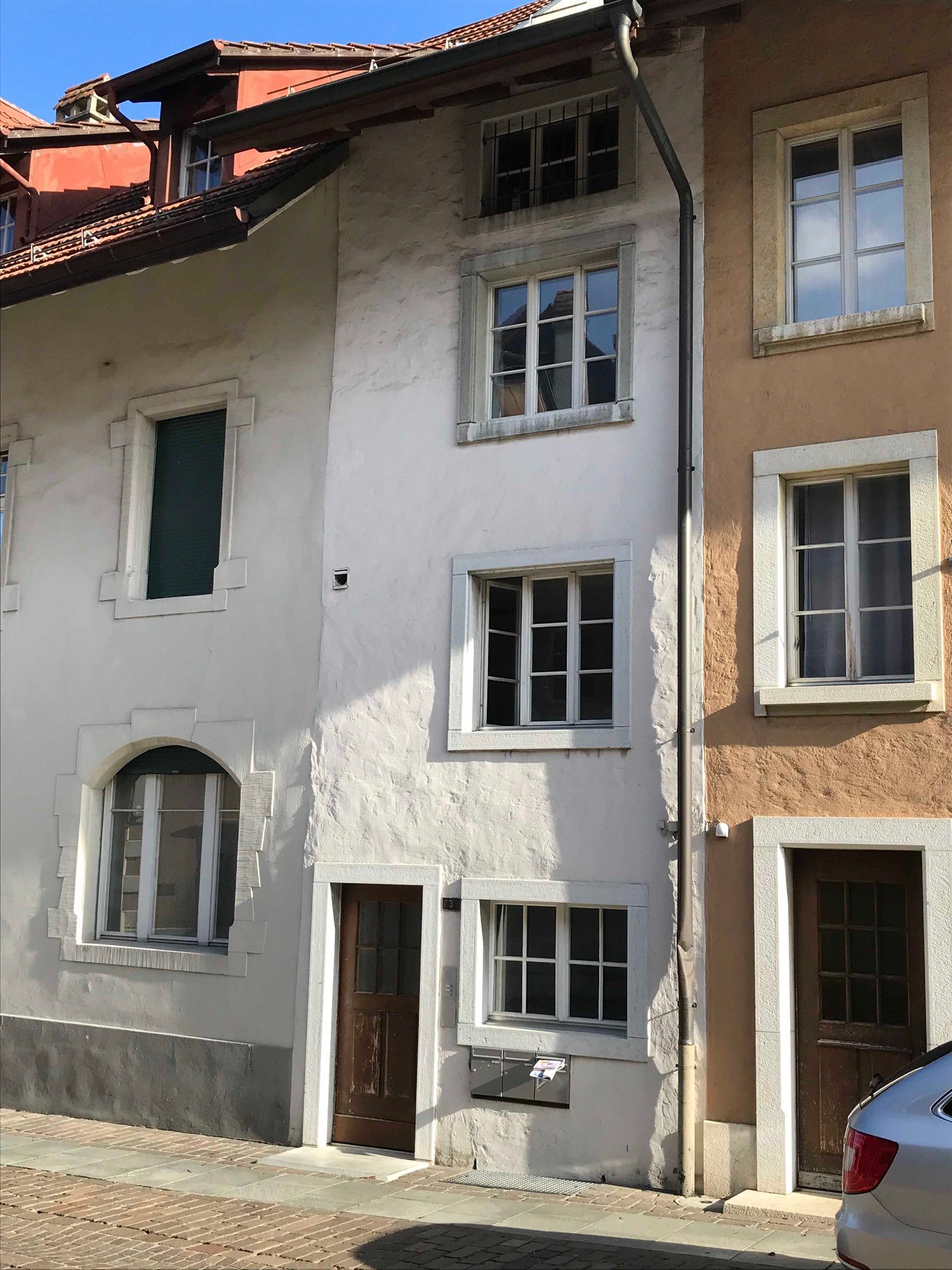 A white building with a brown door, two brown windows, and a brick wall