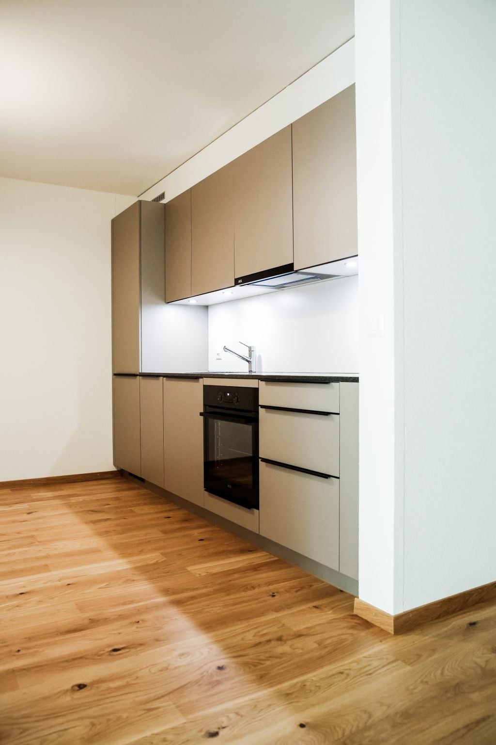 Modern kitchen with wooden floor, brown cabinets, built-in oven, sink with faucet, white walls