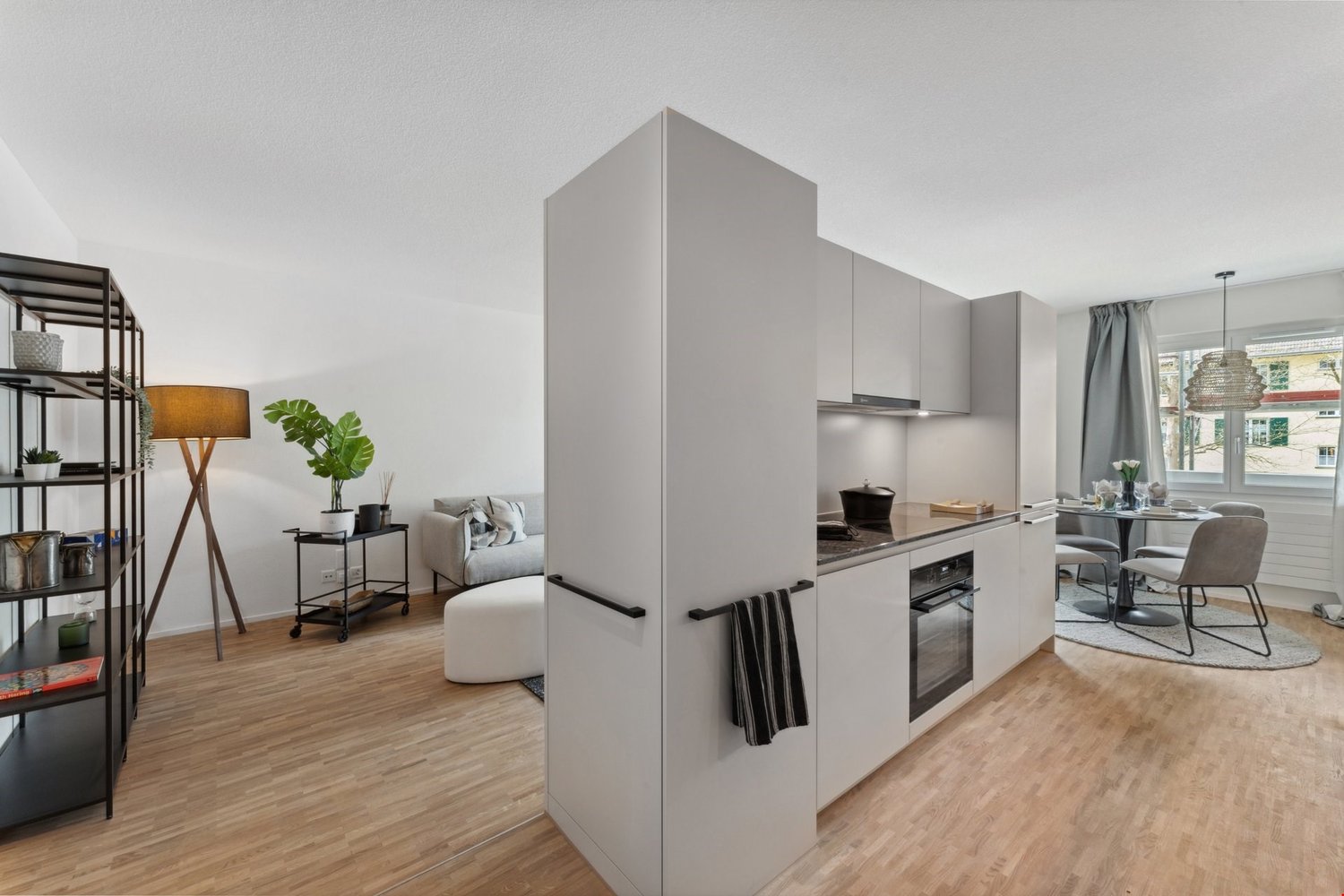 modern, bright living room with wooden floor, kitchen island with a dining table, kitchen equipped with gas stove, oven and refrigerator, white walls, open layout, windows with view