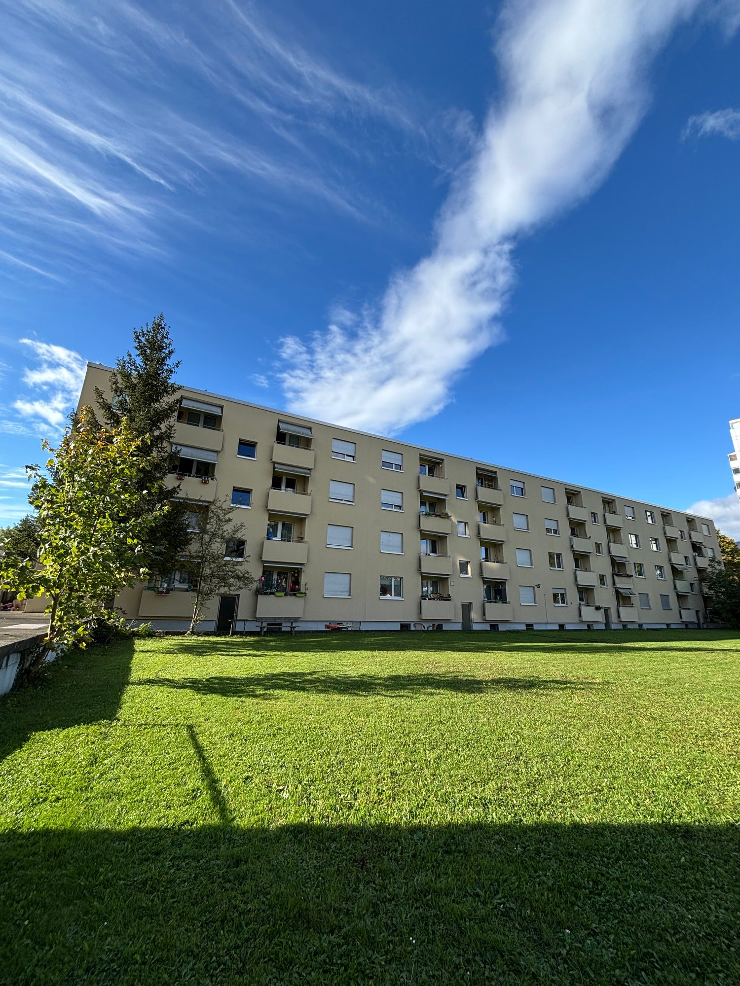 Multi-story apartment building with balconies, surrounded by a well-maintained lawn and trees