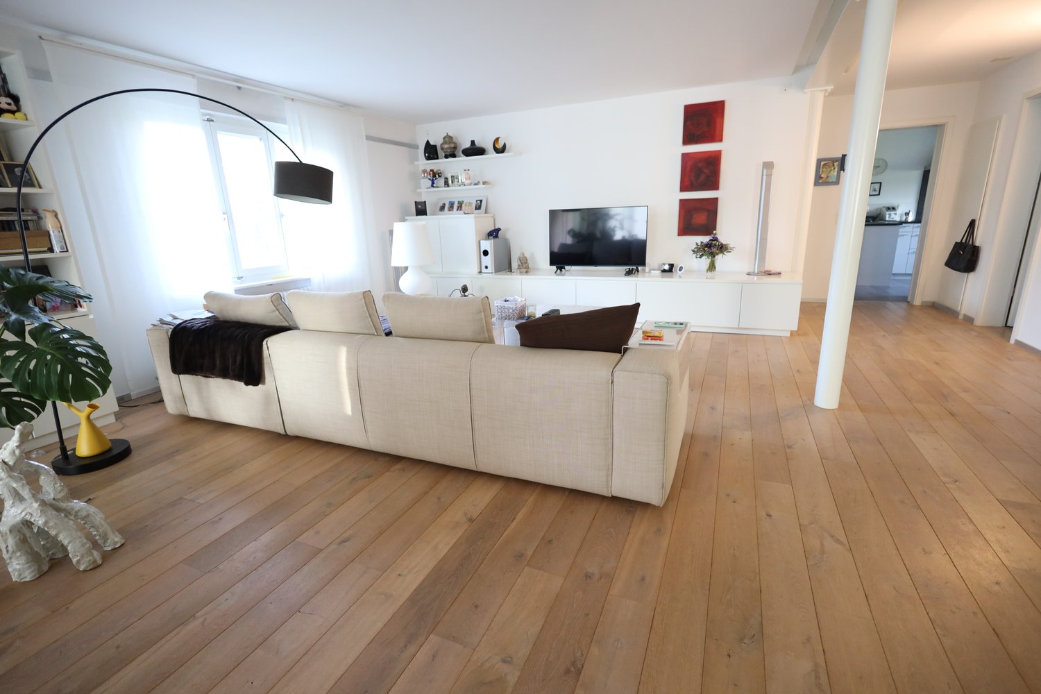 White couch, TV, hardwood floor, lamp, window, shelves with books and decor