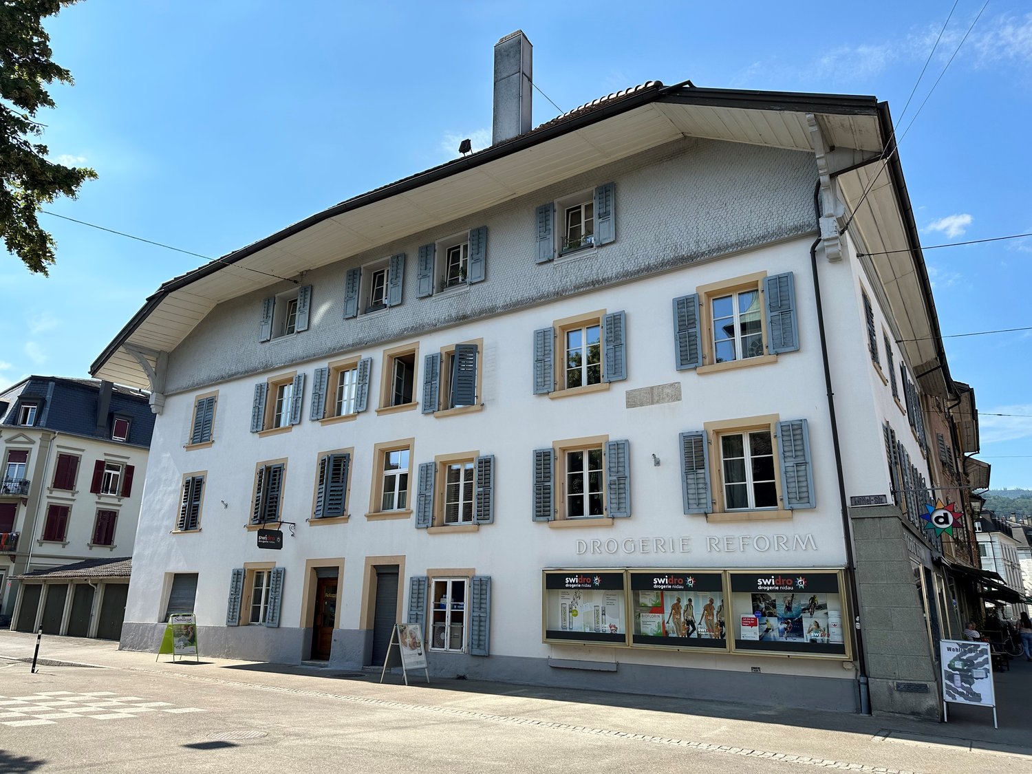 Multistory building, white exterior, multiple windows, arched entrance, tiled roof, sign for DROGERIE REFORM