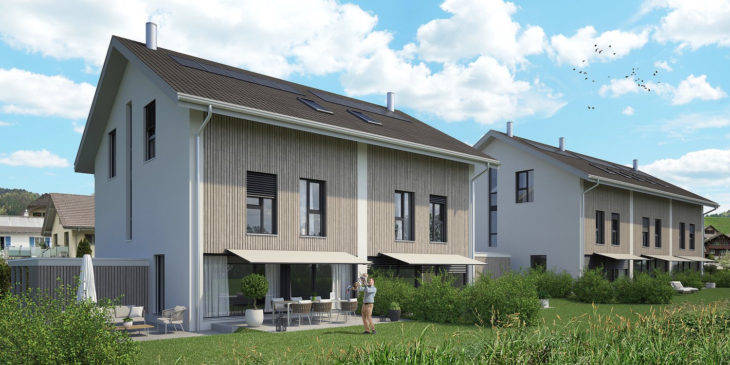 Two-story modern house with gray siding, large windows, and a balcony. The house is surrounded by a grassy yard and has a paved parking area.