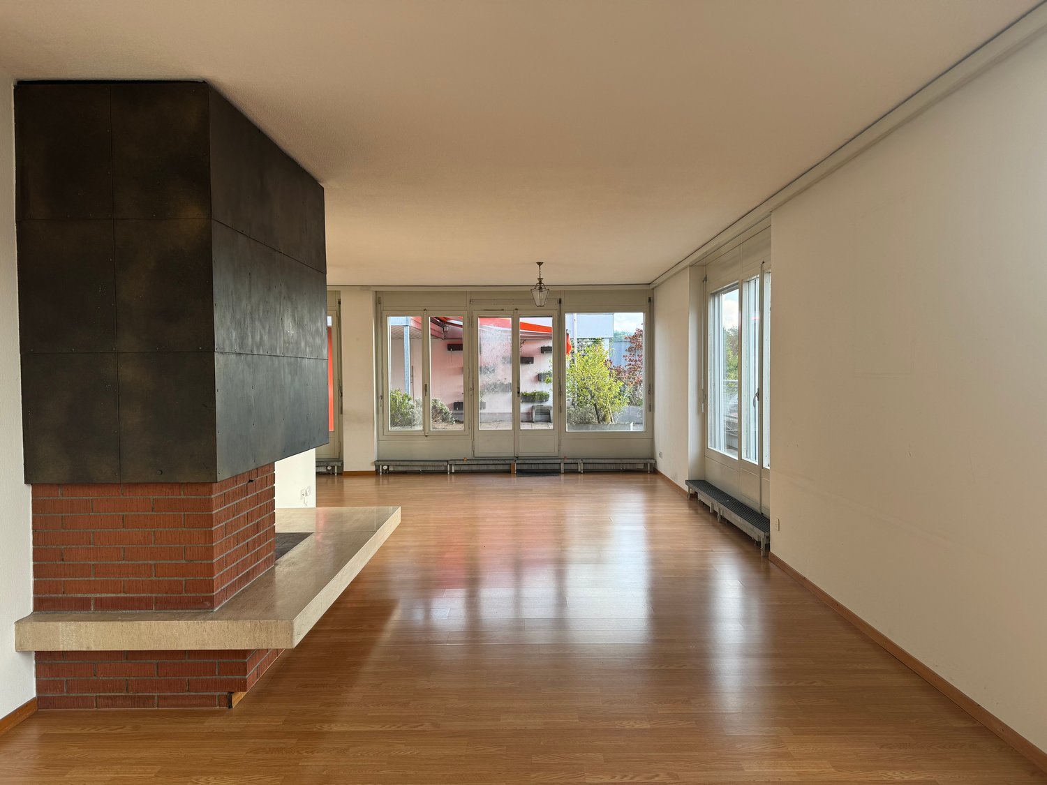 Large open room, brick fireplace, sliding glass doors, wooden floors, white walls