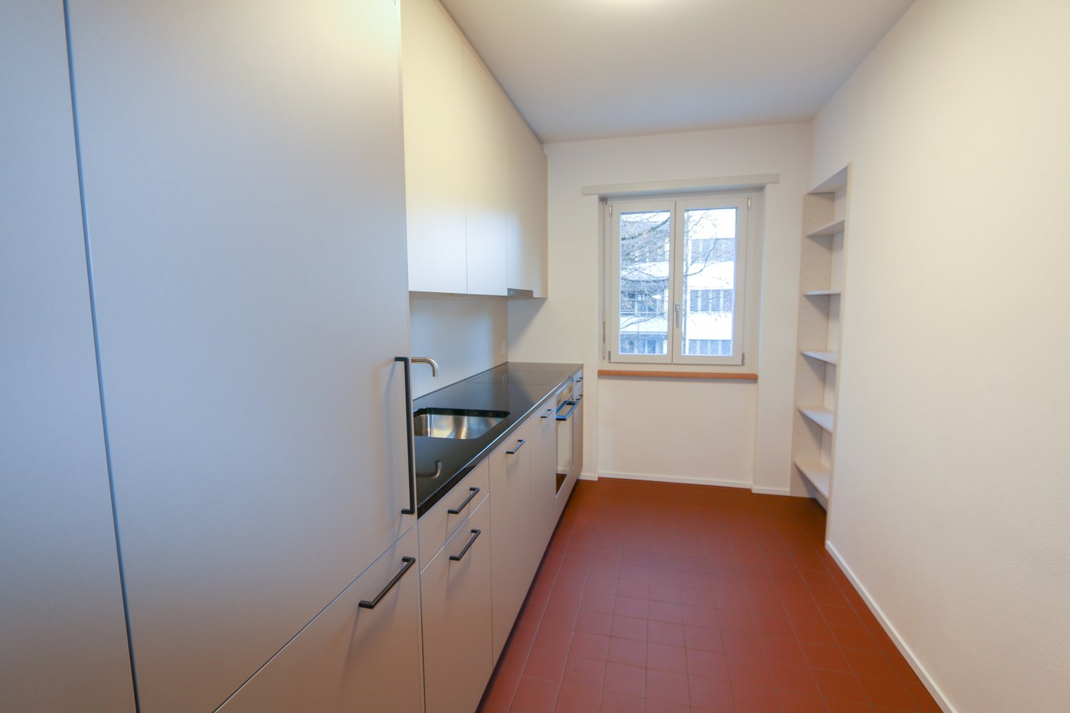 modern kitchen with white cupboards, sink, stove, dishwasher, and red floor tiles