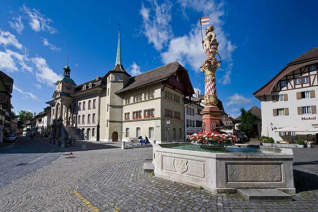 Building with spires, multiple windows, and red flowers, central water fountain, cobblestone street