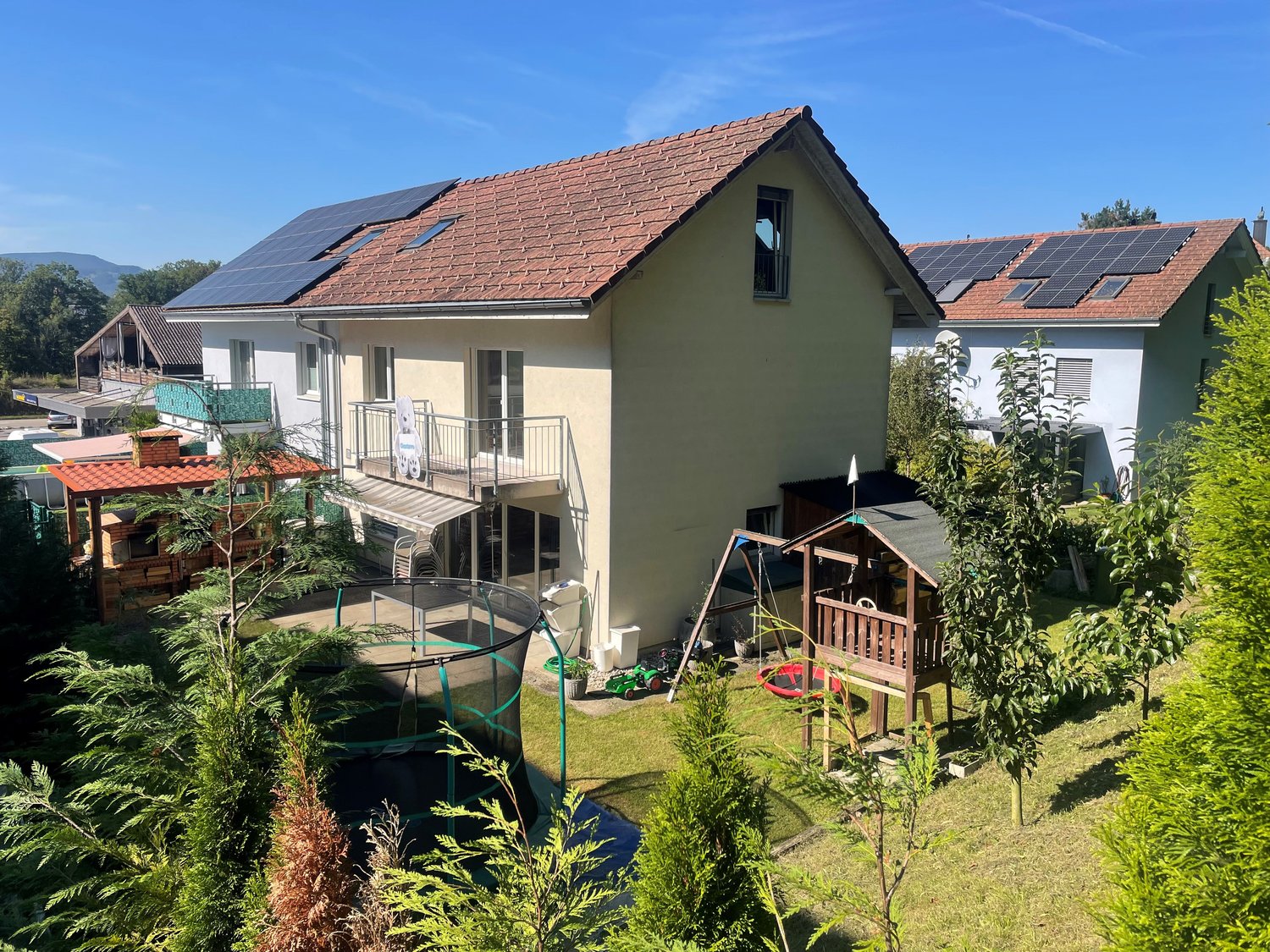 Detached house, red roof, white walls, balcony, solar panels, yard, playground, garden shed, trampoline, swing, slide, barbecue