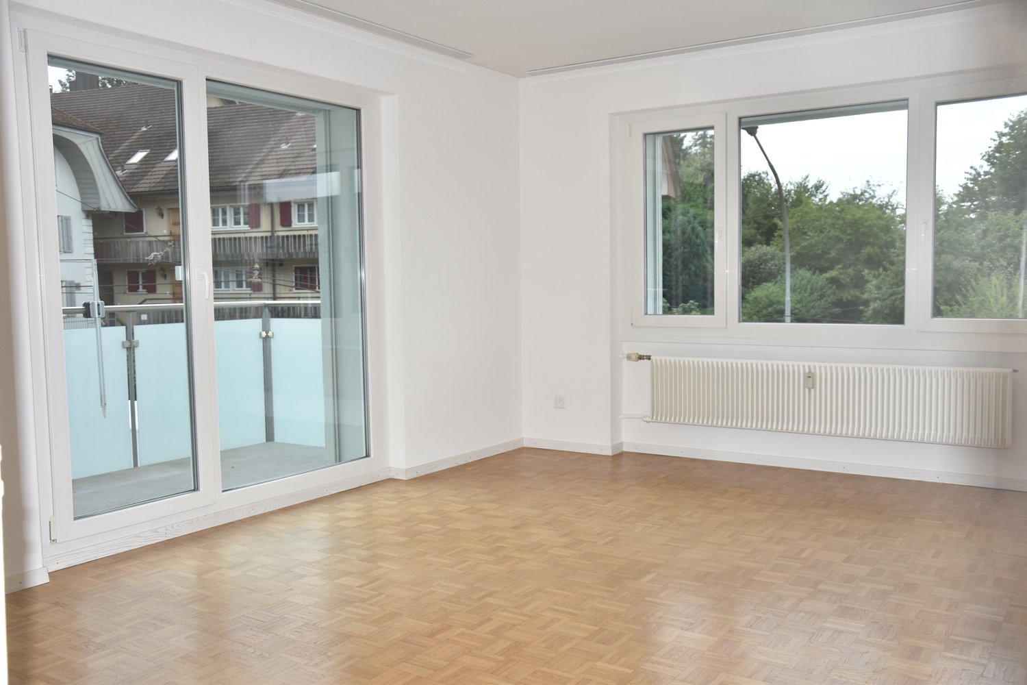empty room, hardwood floor, glass sliding doors, windows, white walls, radiator, balcony