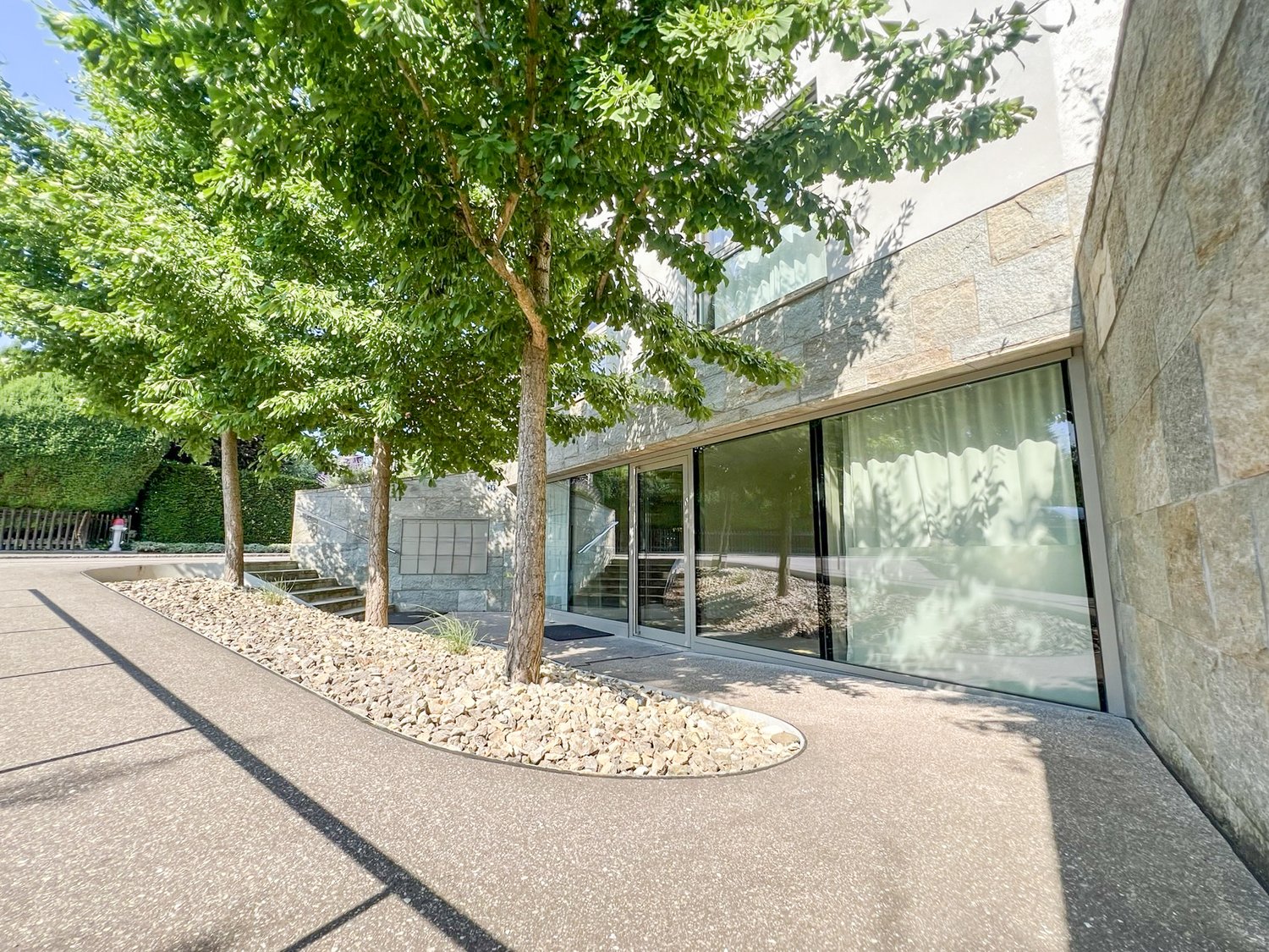Modern stone building with glass walls and staircases, surrounded by well-maintained landscaping