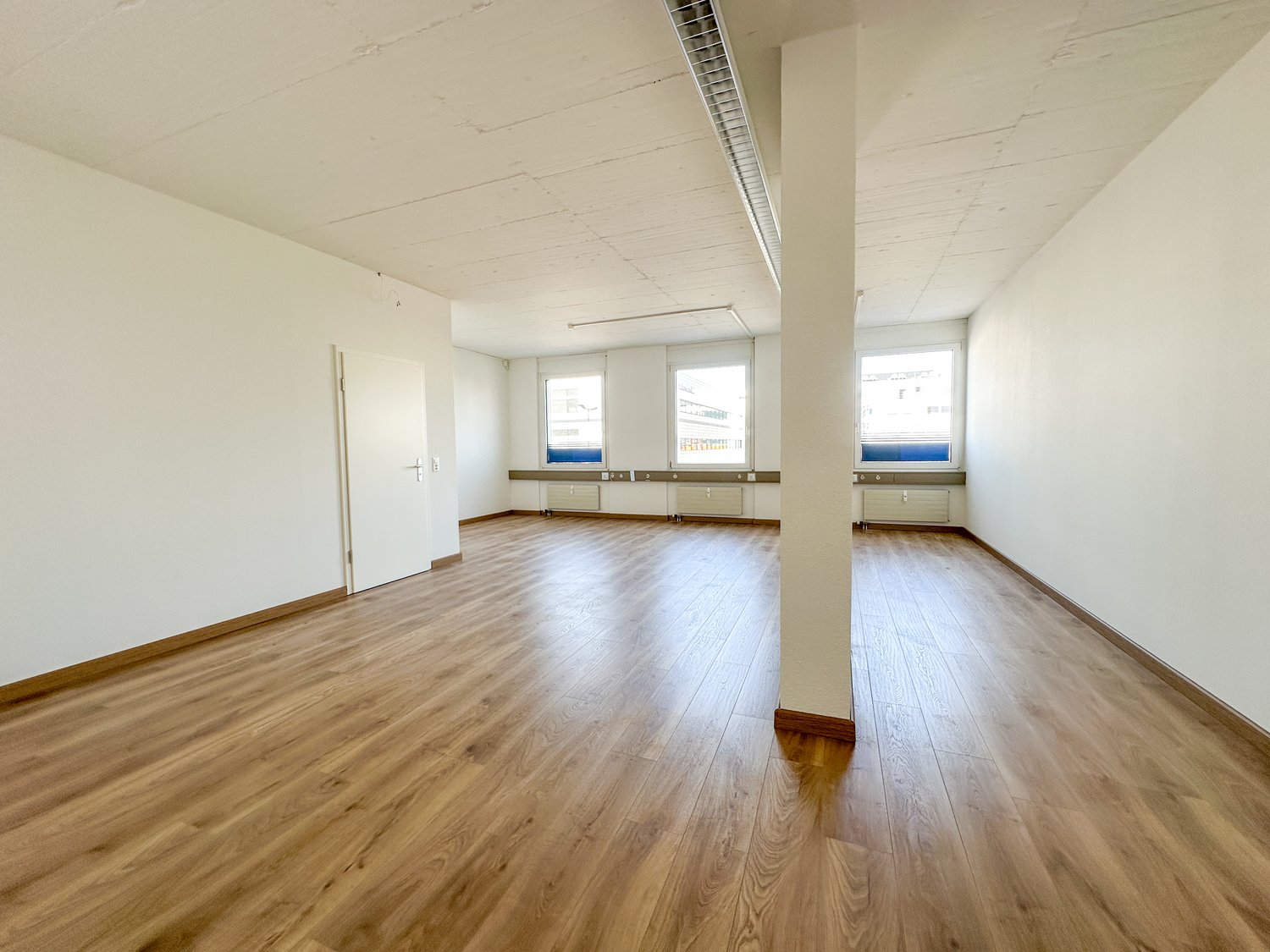 empty room, wooden floor, white walls, three windows, central pillar, white door
