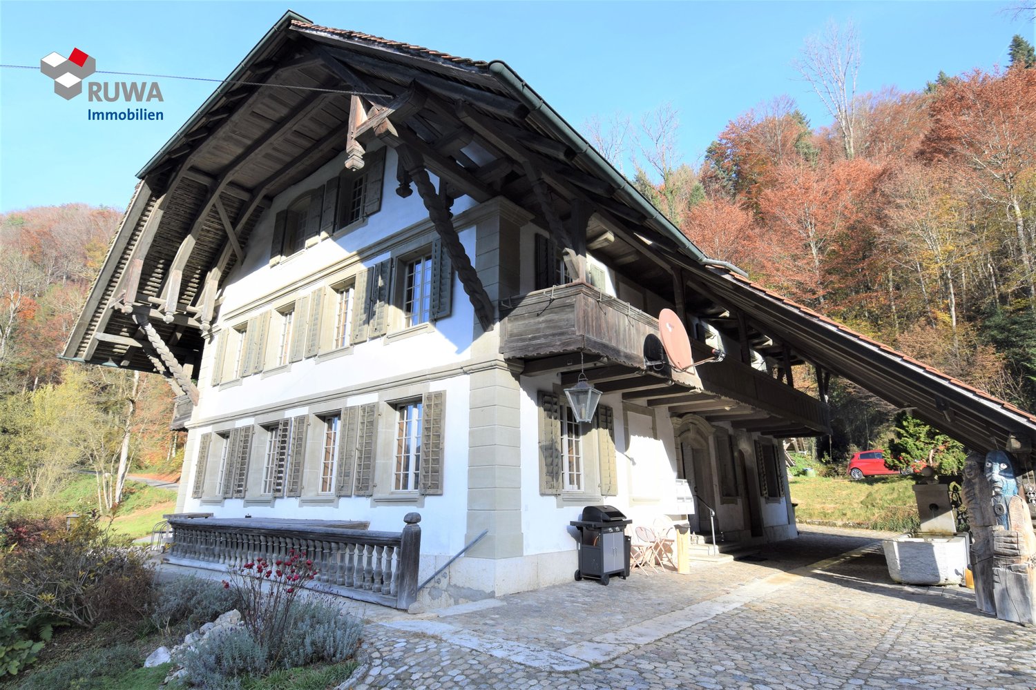 2 story house, white exterior, green shutters, large porch, wooden balcony, tiled roof, small garden with plants, surrounded by trees