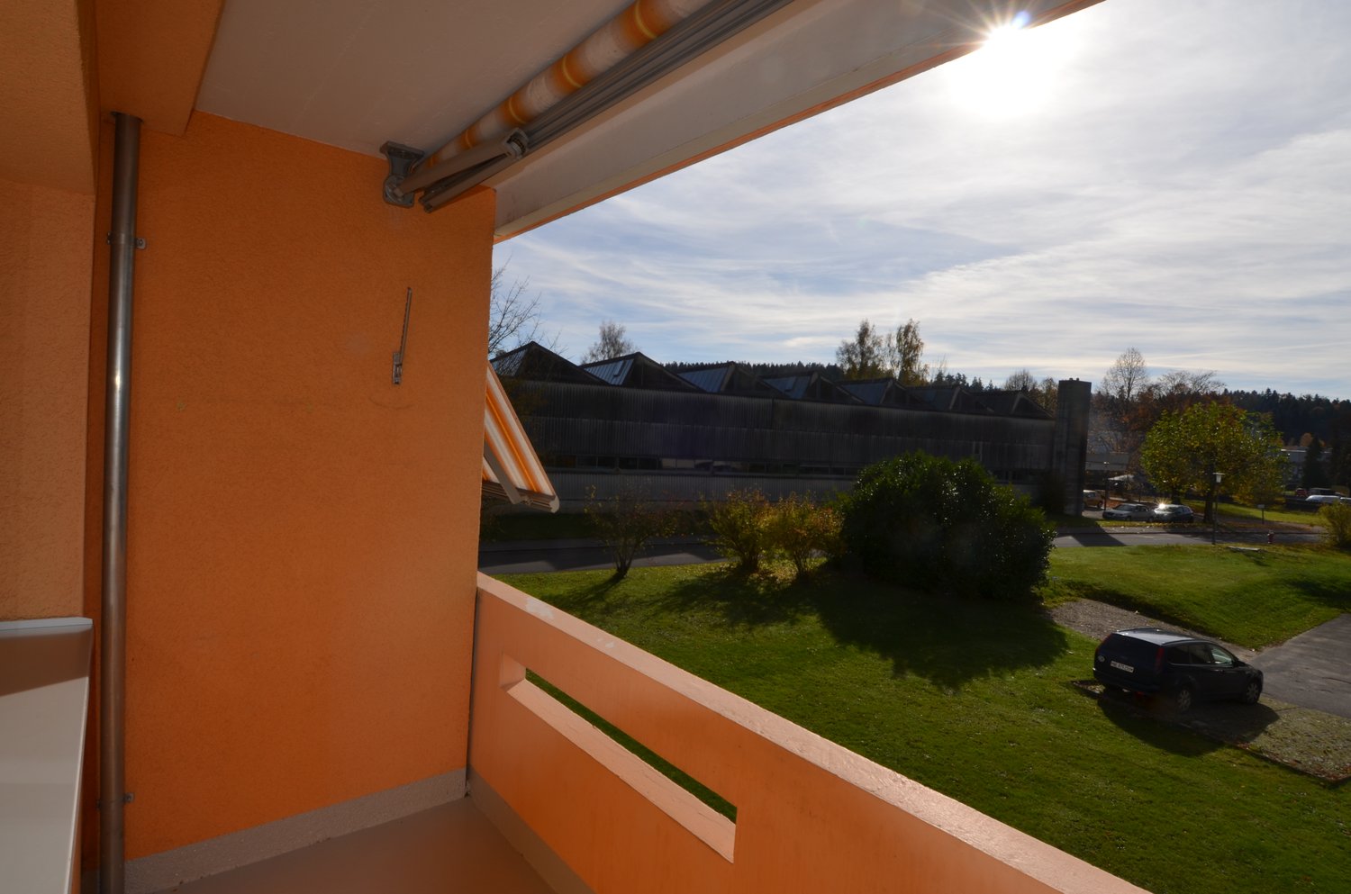bright room with a balcony, view of a car park and greenery, orange wall