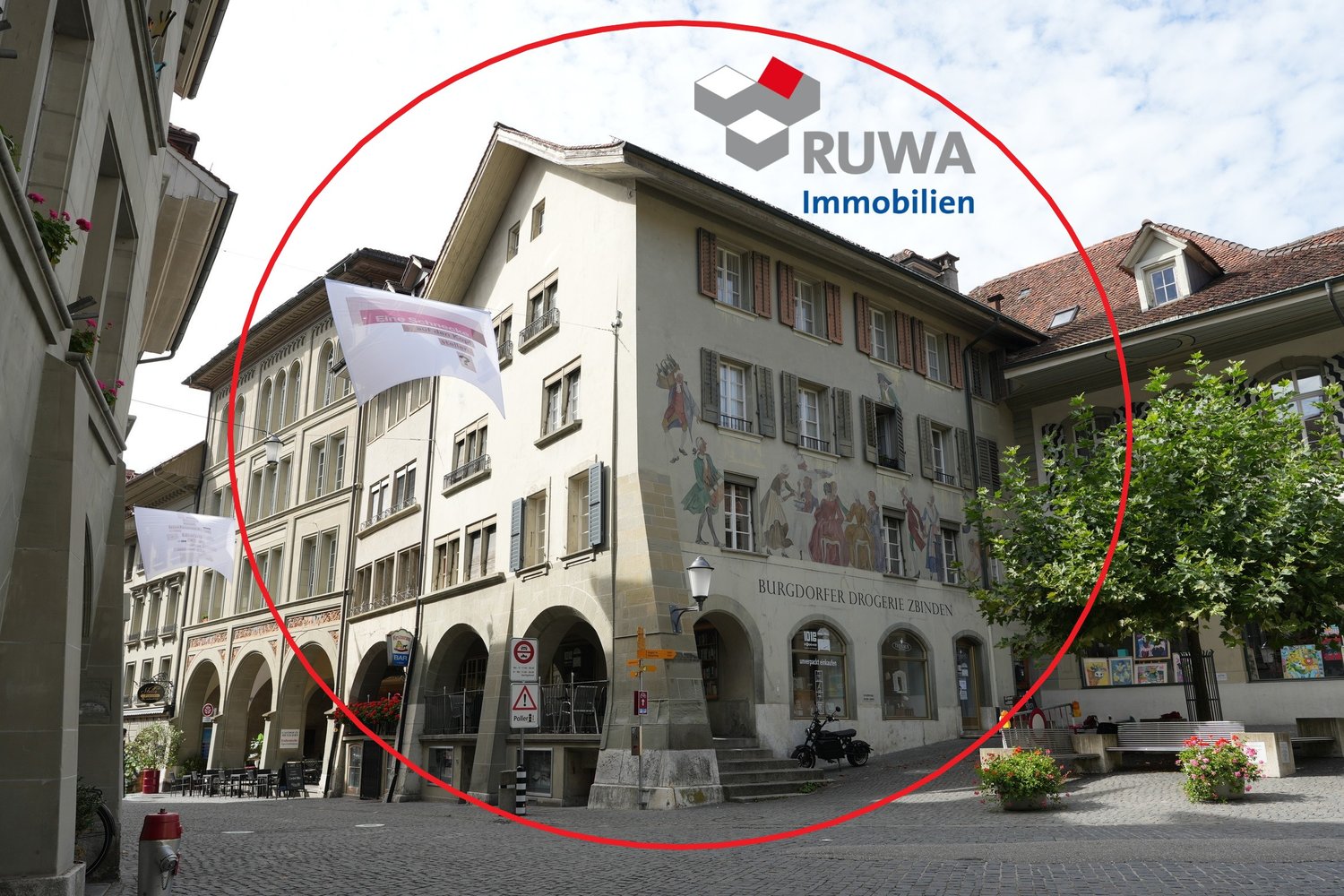 Historic building, arched entrance, murals, red awning, terrace, parked motorcycle, street-level shops