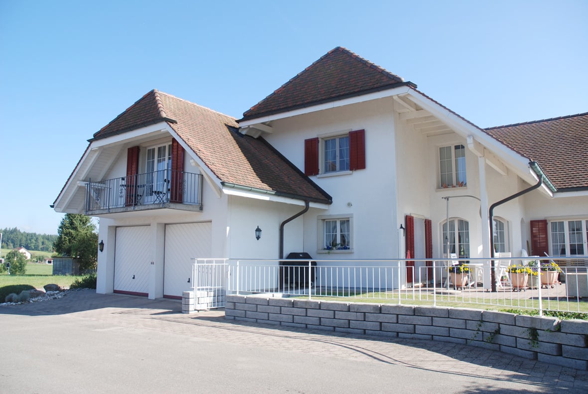 2-story house, white painted, brown roof, balcony, double garage, fenced yard, garden, patio, outdoor seating, grill, wall lamps