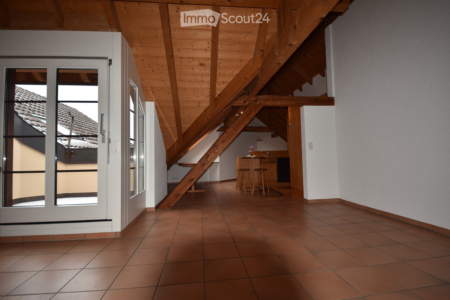 Wooden ceiling, kitchen with bar stools and counter, white walls, tiled floor, glass door