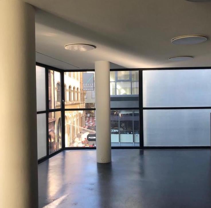 Large room, high windows, modern design, central pillar, grey floor, glass windows, reflective surfaces