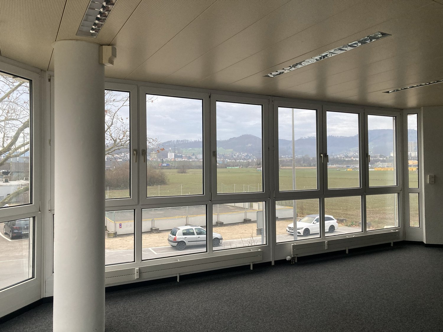 Wide windows, empty room, view of vehicles in parking area