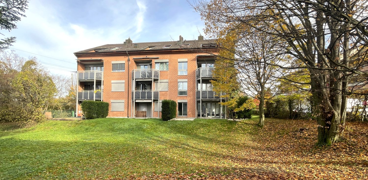 2 story brick building, windows with shutters, glass doors on balconies, landscaped garden