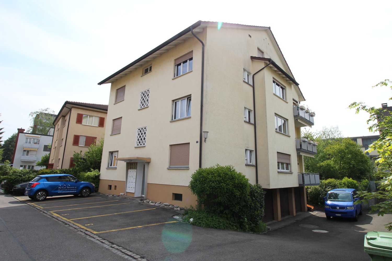 multi-story building, beige and brown exterior, cars parked in front, balconies, mailboxes