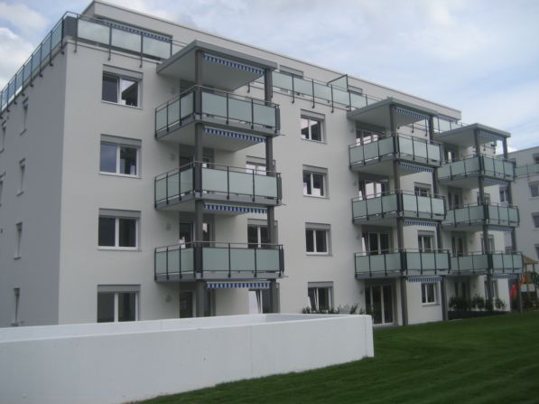 4-story apartment building with multiple balconies, glass windows, and a grassy area in front