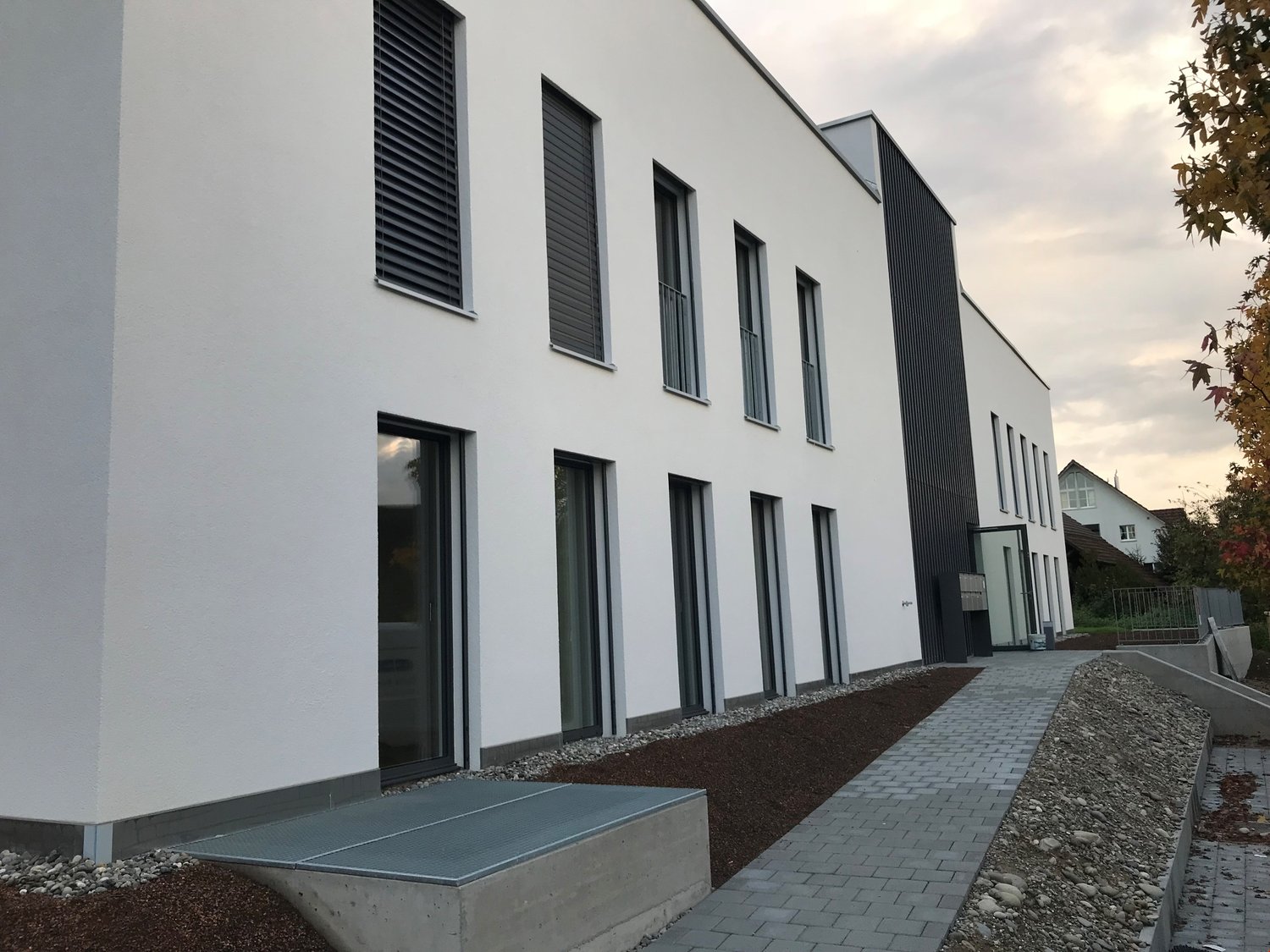 white and black exterior, several windows, entrance with glass doors, brick footpath