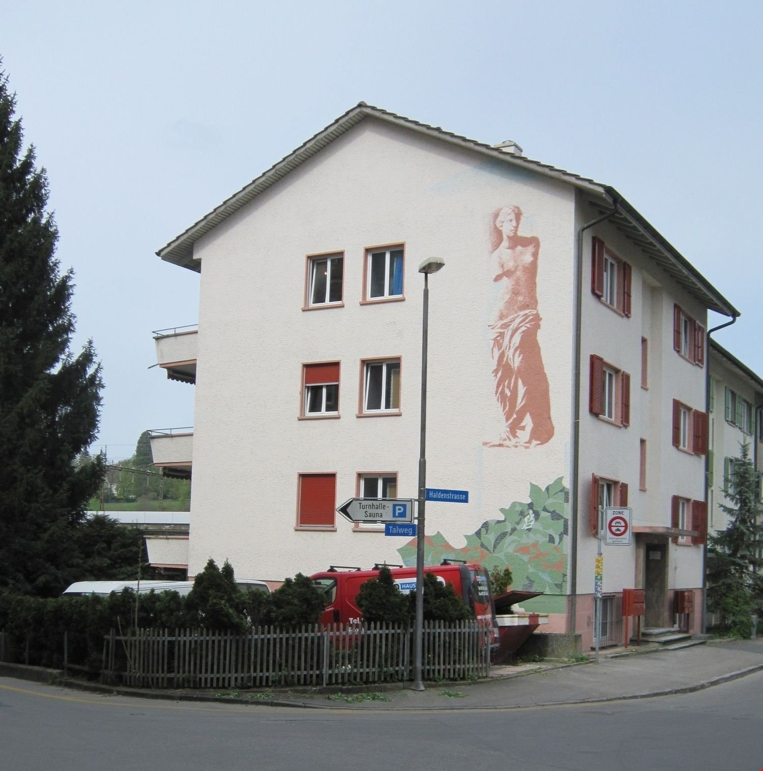 2 story white building, red shutters, street lamp, no visible balconies, red delivery truck parked in front, mailbox at the entrance