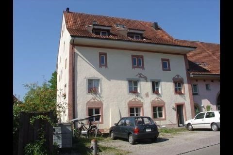 Two-story house with white walls, brown roof, multiple windows, cars parked in front, a bicycle propped against the building
