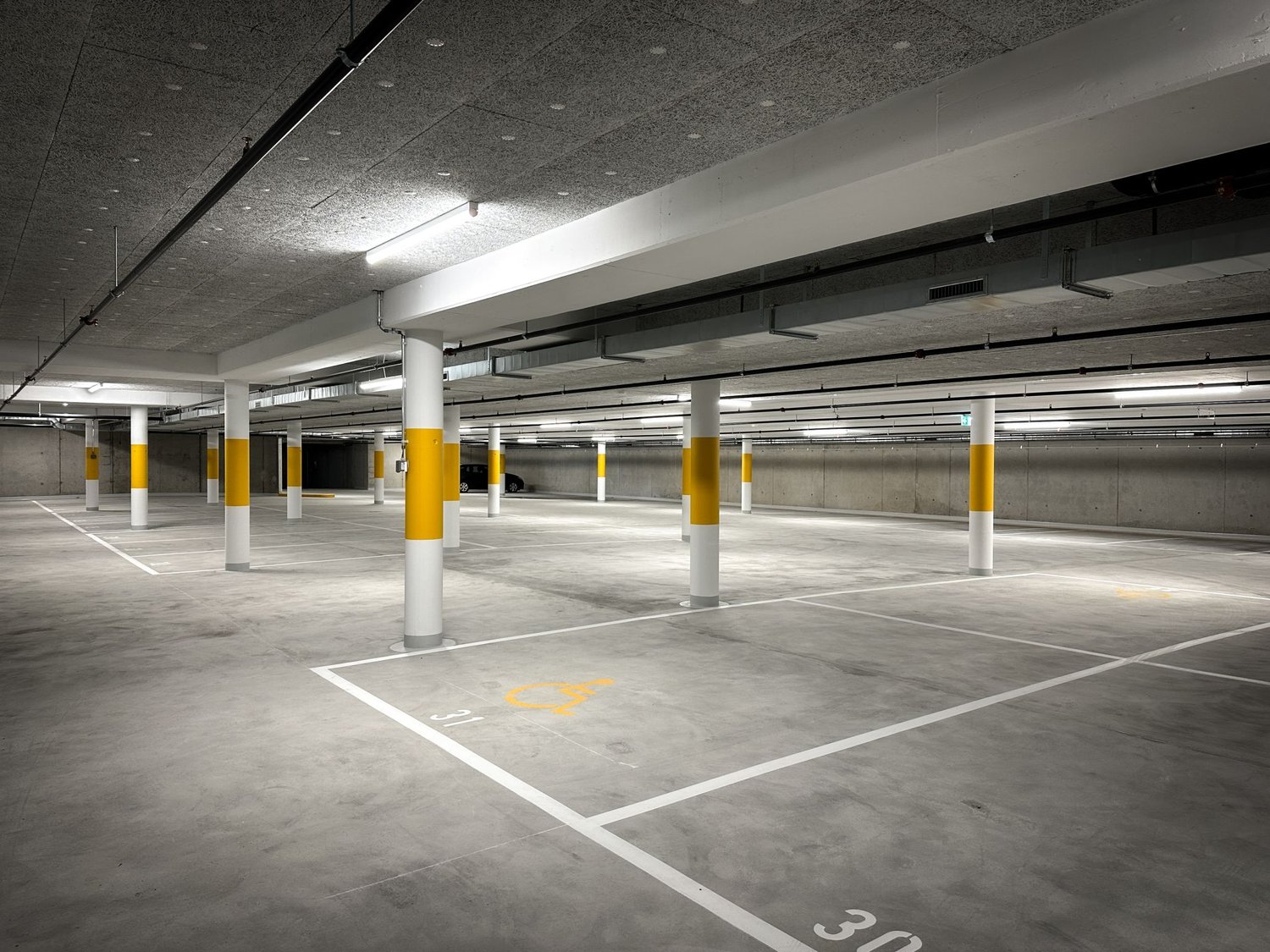 Concrete floor, yellow and white columns, designated parking spaces, disabled parking symbol, white lines marking parking spots, fluorescent lighting.