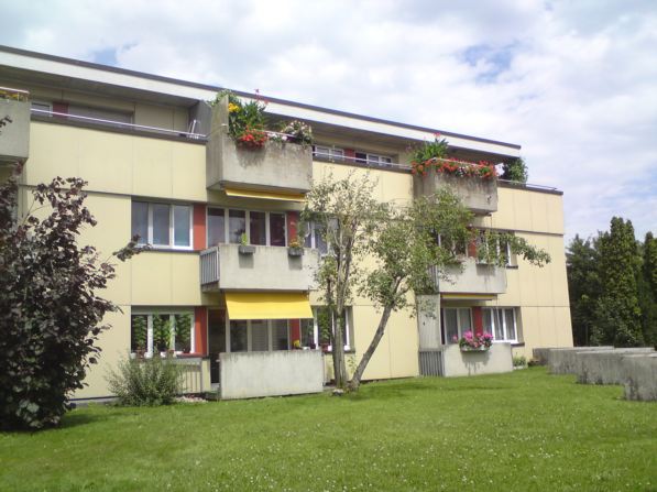 3 story building, yellow and white facade, balconies, trees and shrubs, grassy area