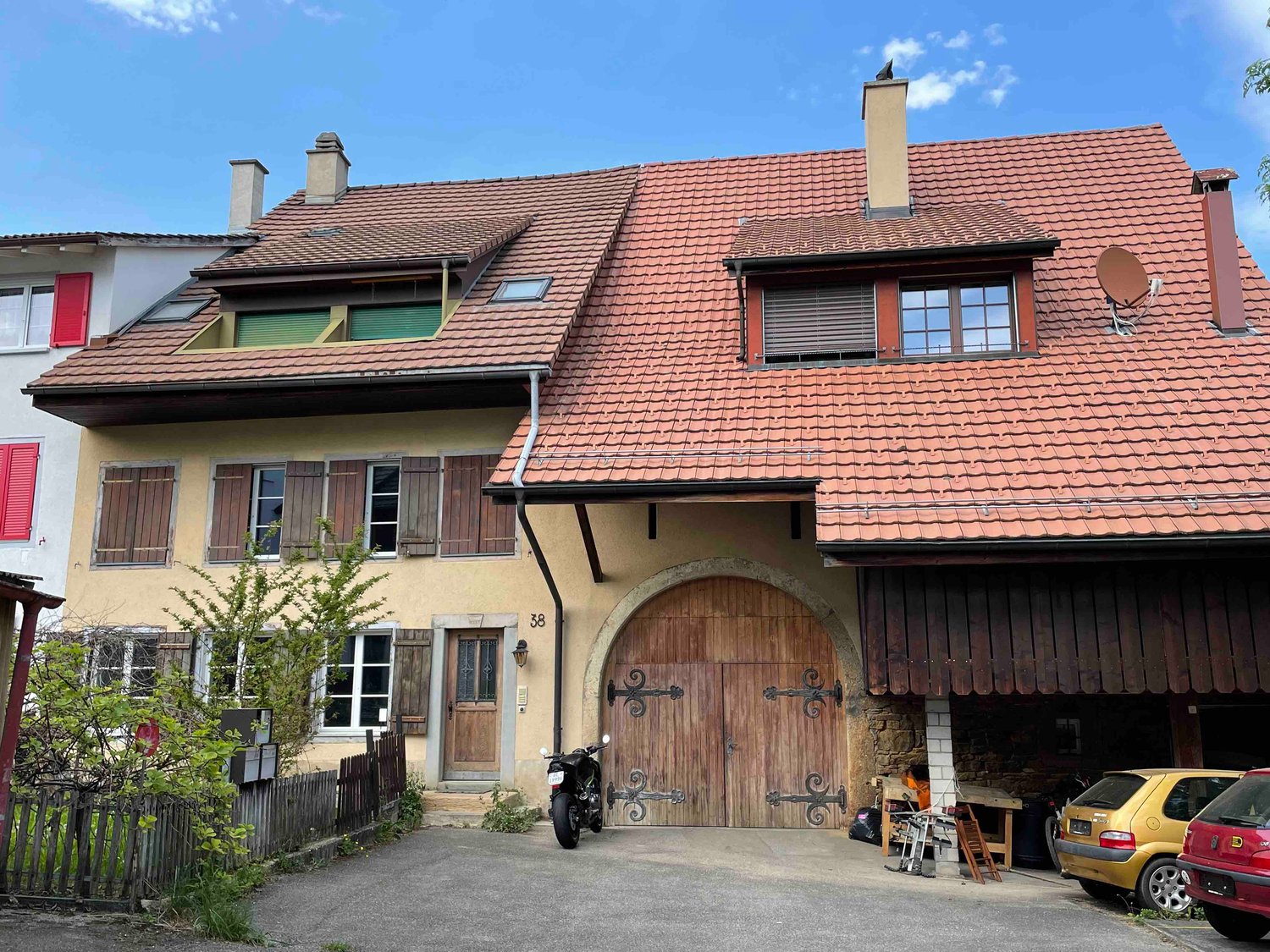 yellow facade, large arched wooden door, tiled roof, two cars and a motorcycle parked