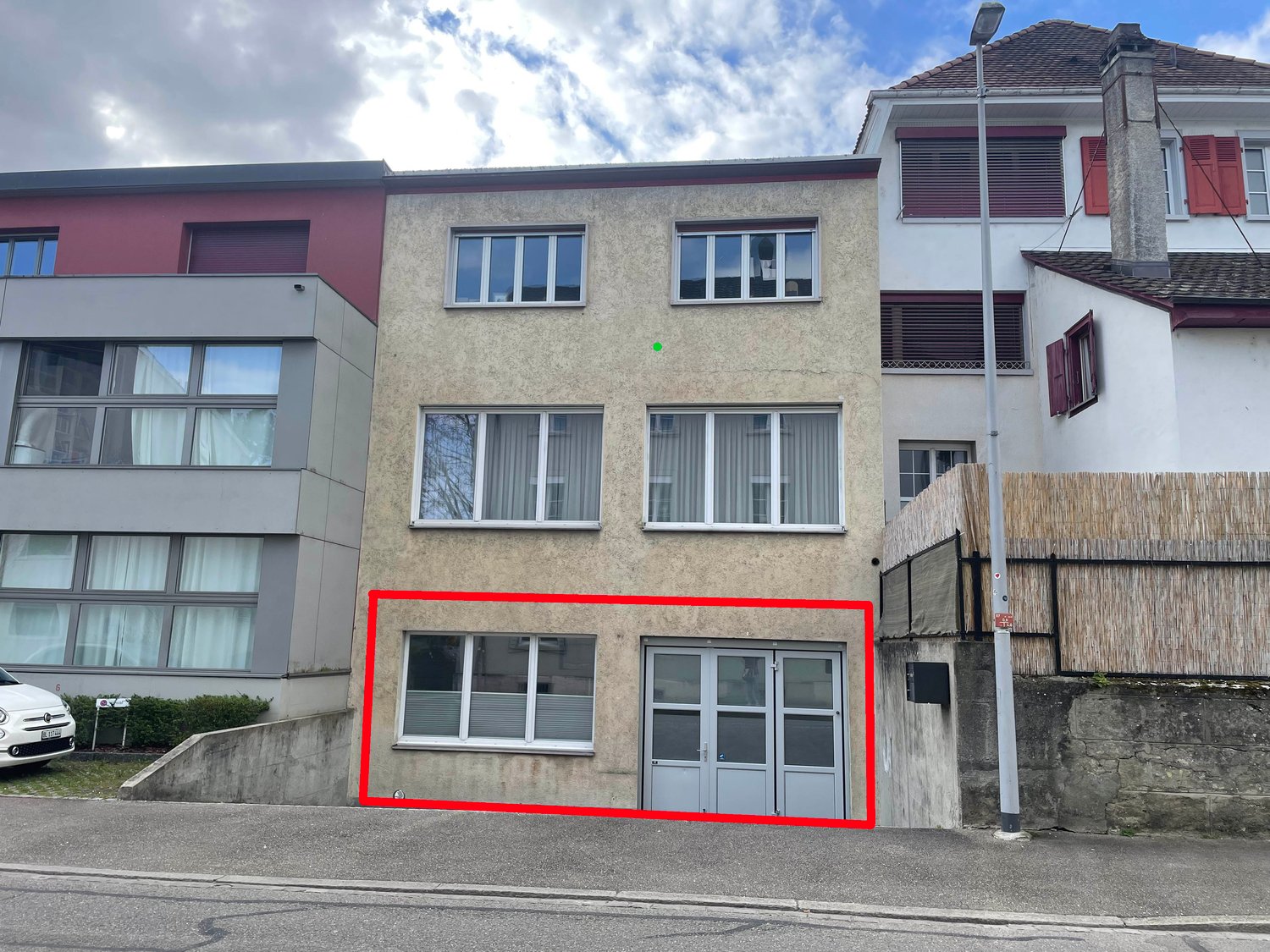 3-story building, concrete walls, glass windows, double doors, red outline highlighting the entrance area