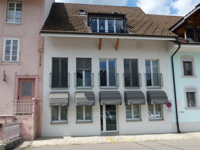 white building, brown roof, multiple windows, balconies, awnings, entrance door