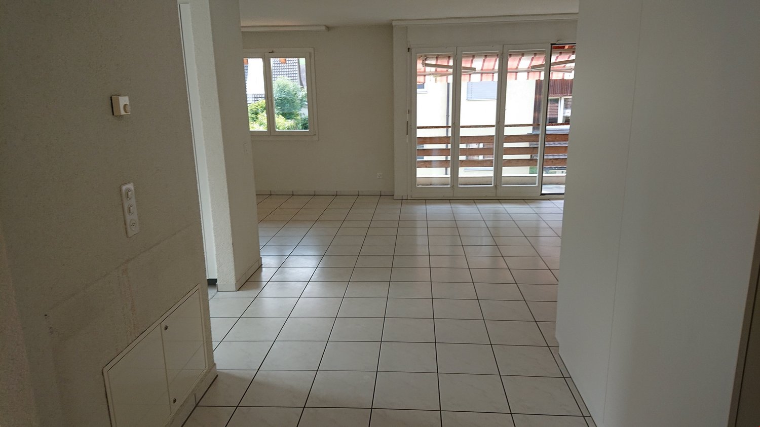 empty room with white tiles and sliding glass doors leading to balcony