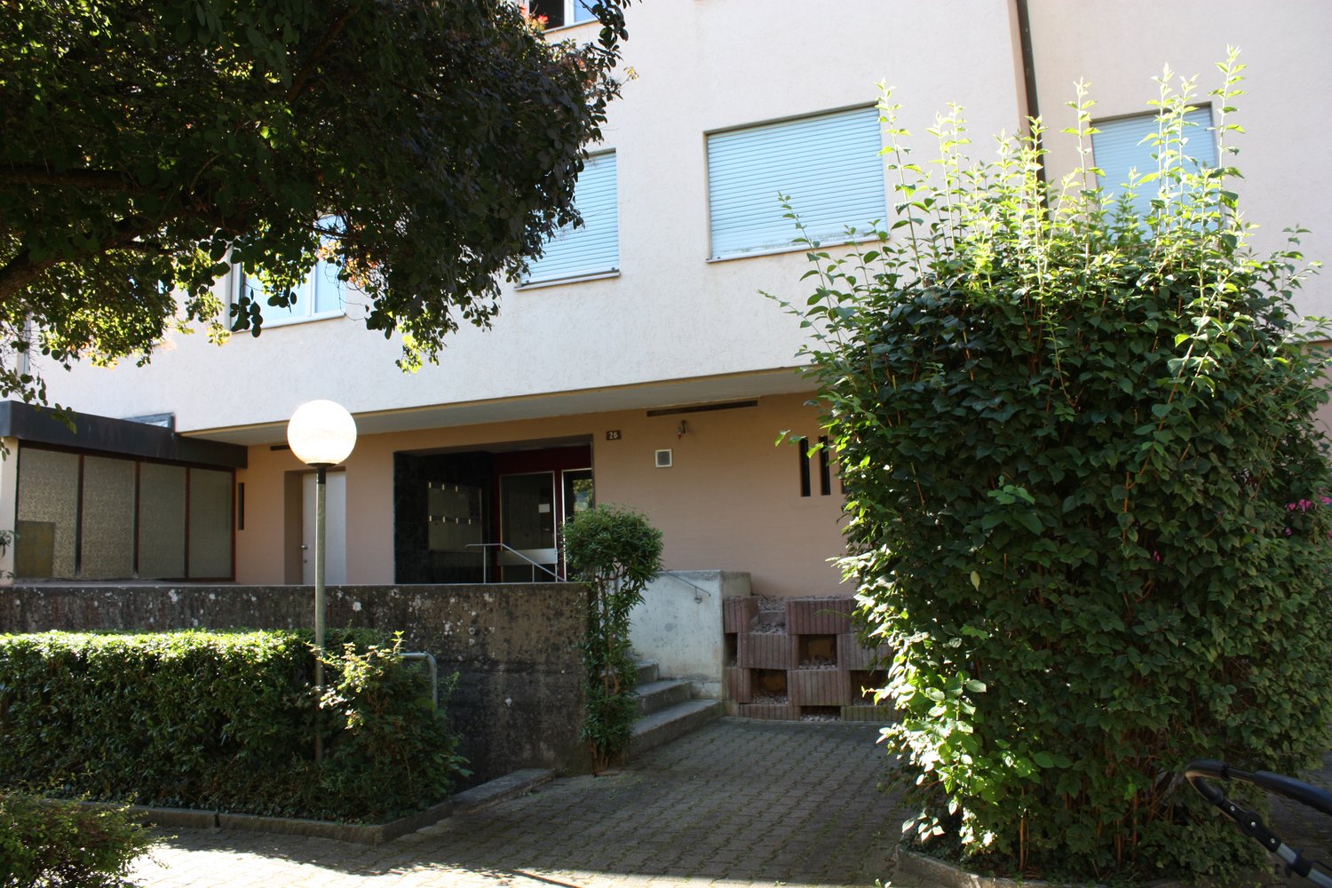 White building with several windows, outdoor area with a lamp, staircase and small hedges