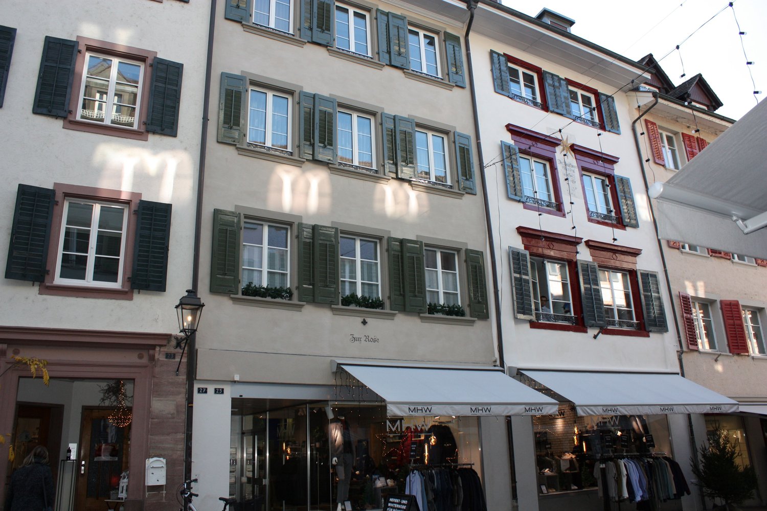 3 story building, white walls, green shutters, red trim, multiple windows, shops on the ground floor
