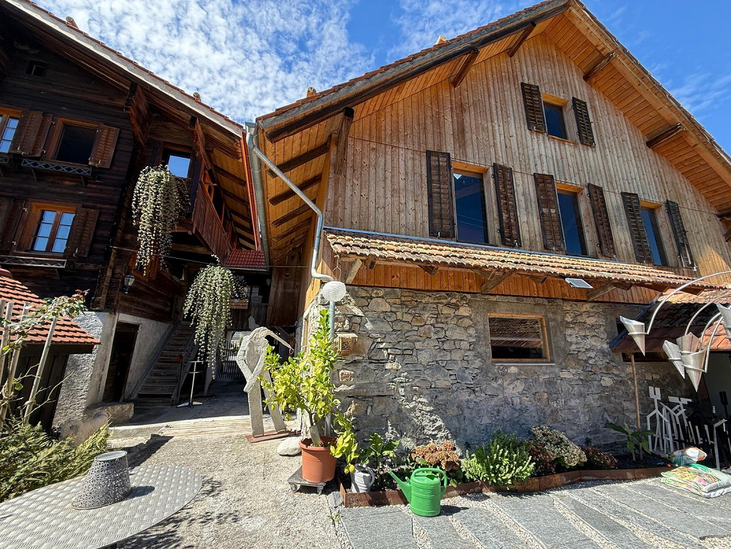 2 story wooden building, stone bottom floor, roof terrace, windows with shutters, plants, garden