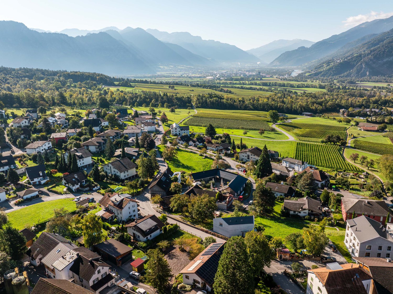 Small town with many houses, surrounded by green fields, hills, and mountains