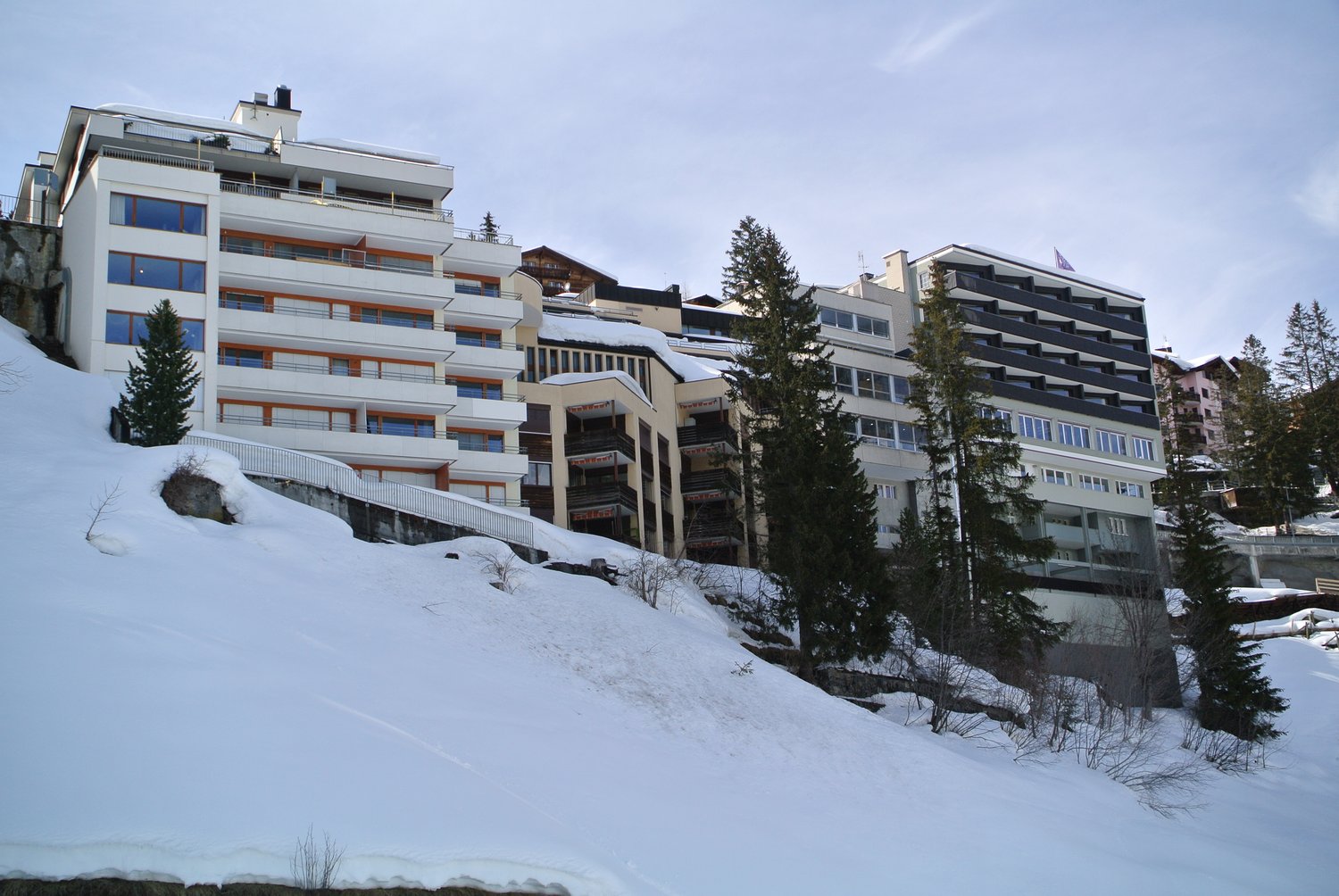 large white apartment building with glass windows overlooking snow covered mountain