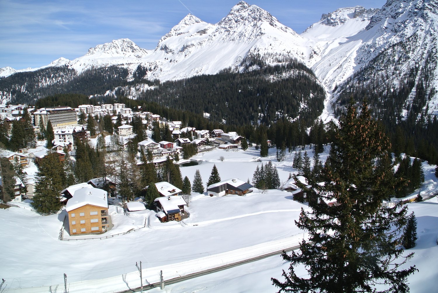 Mountain village, multiple chalets, covered in snow, pine trees, expansive mountains