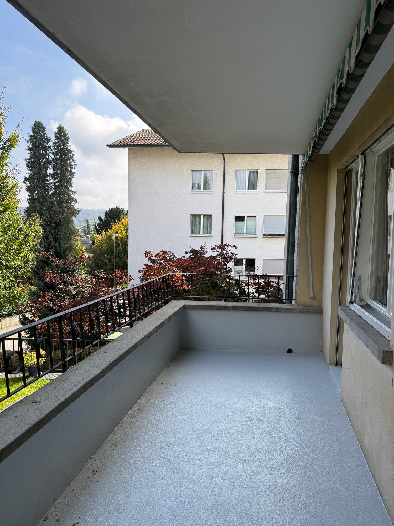 empty balcony, black railings, white floor, green striped awning