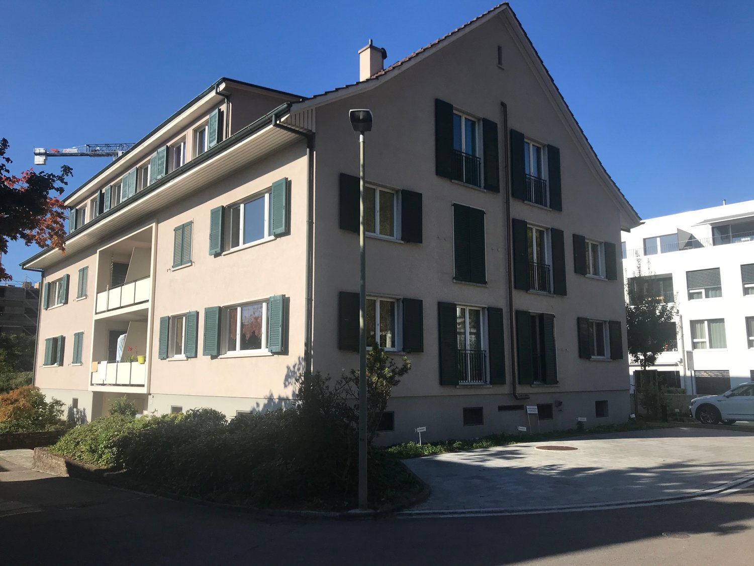 4 story apartment building, multiple balconies, green shutters, white windows, parking area