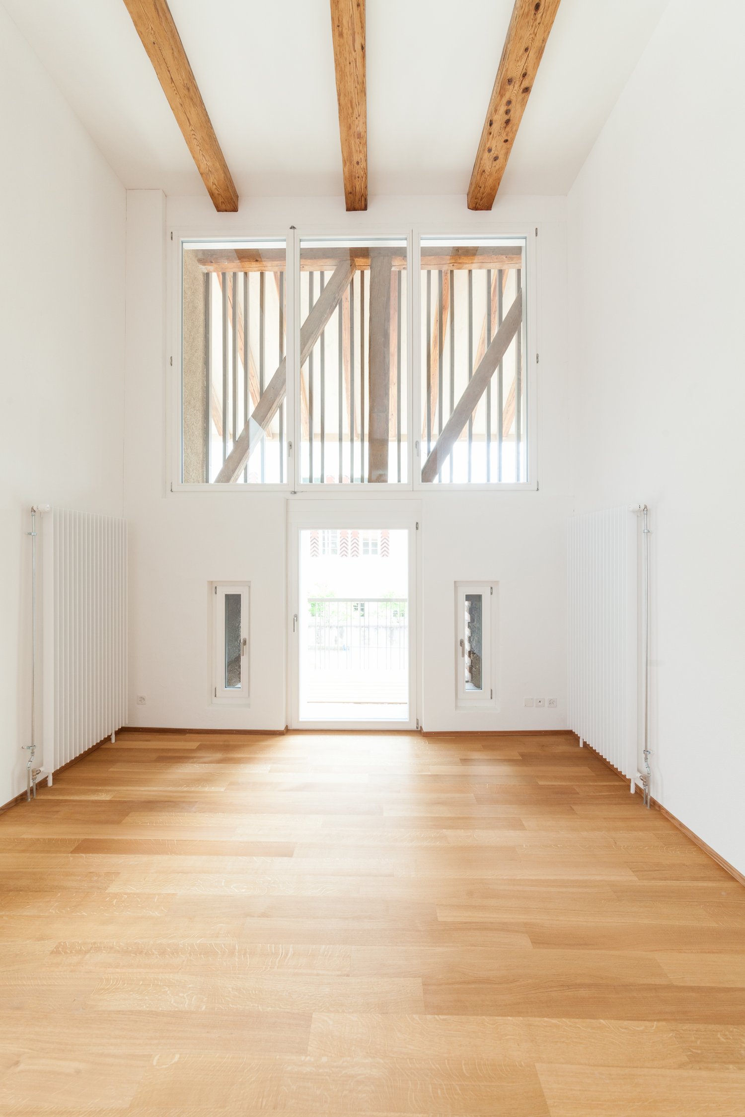 large open space, wooden floor, high ceiling with exposed wooden beams, large glass windows with balcony